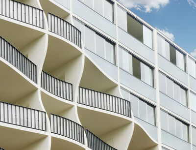 Fassade eines modernen Wohngebäudes mit wellenförmigen Balkonen und minimalistischen Glasfronten.