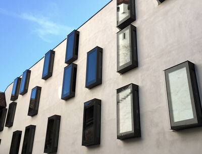 Nahaufnahme einer modernen Fassade mit unregelmäßig angeordneten, rechteckigen Fenstern, die aus der Wand herausragen und eine interessante, versetzte Anordnung bilden.