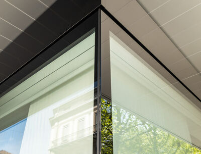 Nahaufnahme einer Gebäudeecke mit großen, reflektierenden Glasfassaden.